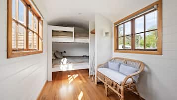 A room with a bunk bed, a wicker chair, and large windows.