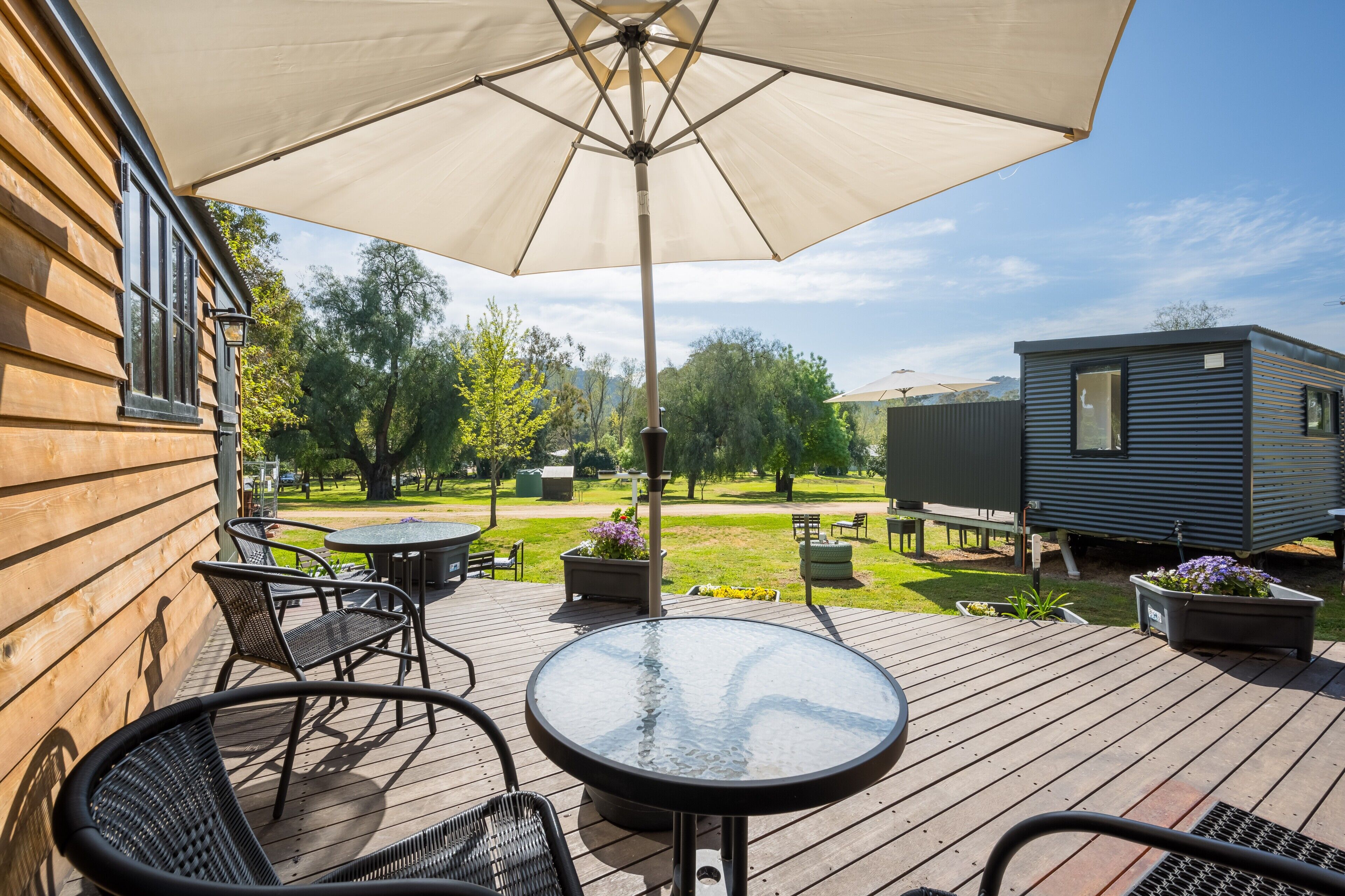 A wooden deck with outdoor furniture, a glass table, and a large umbrella.