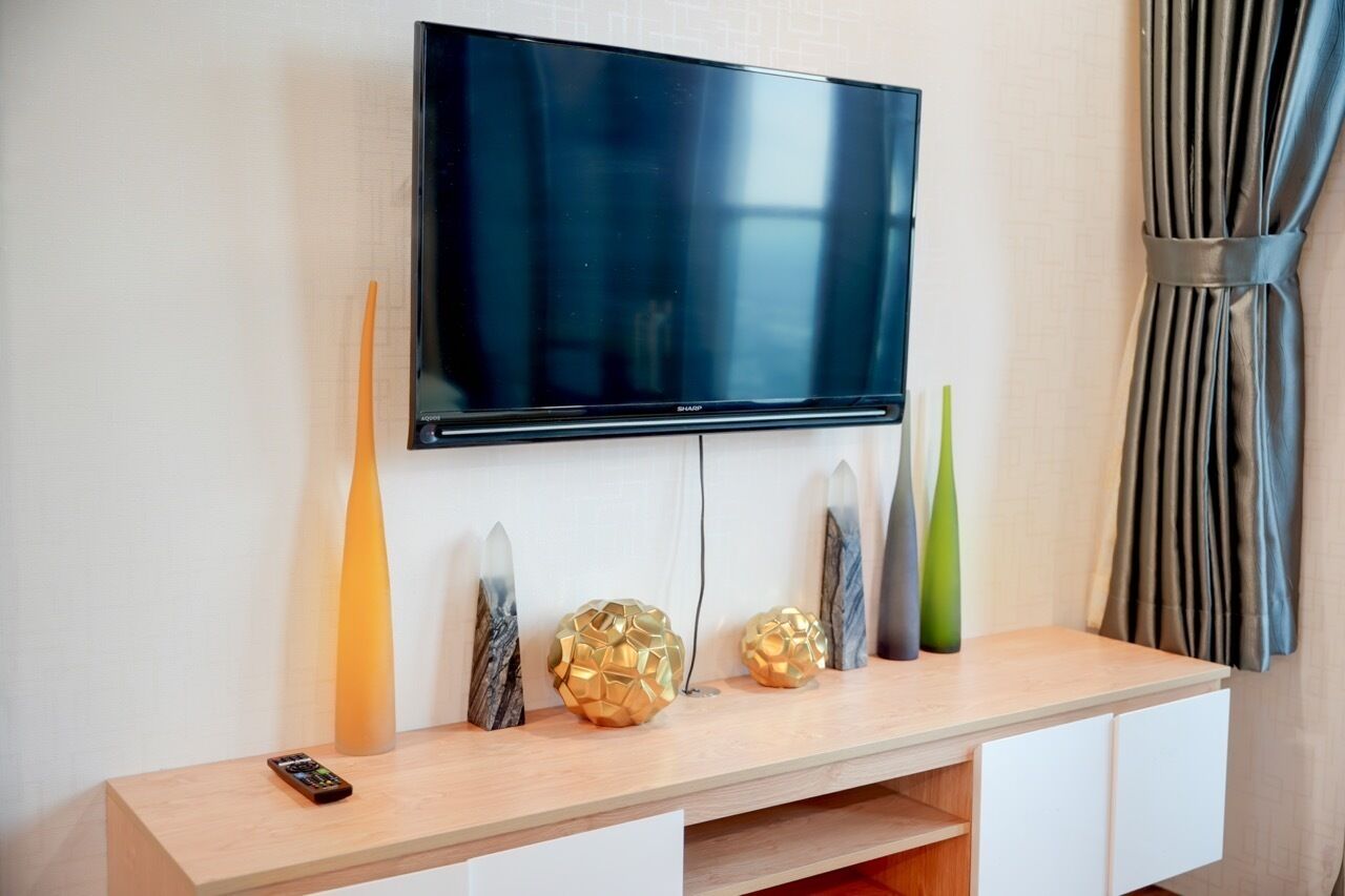 A flat-screen TV mounted on a wall above a wooden console with decorative items.