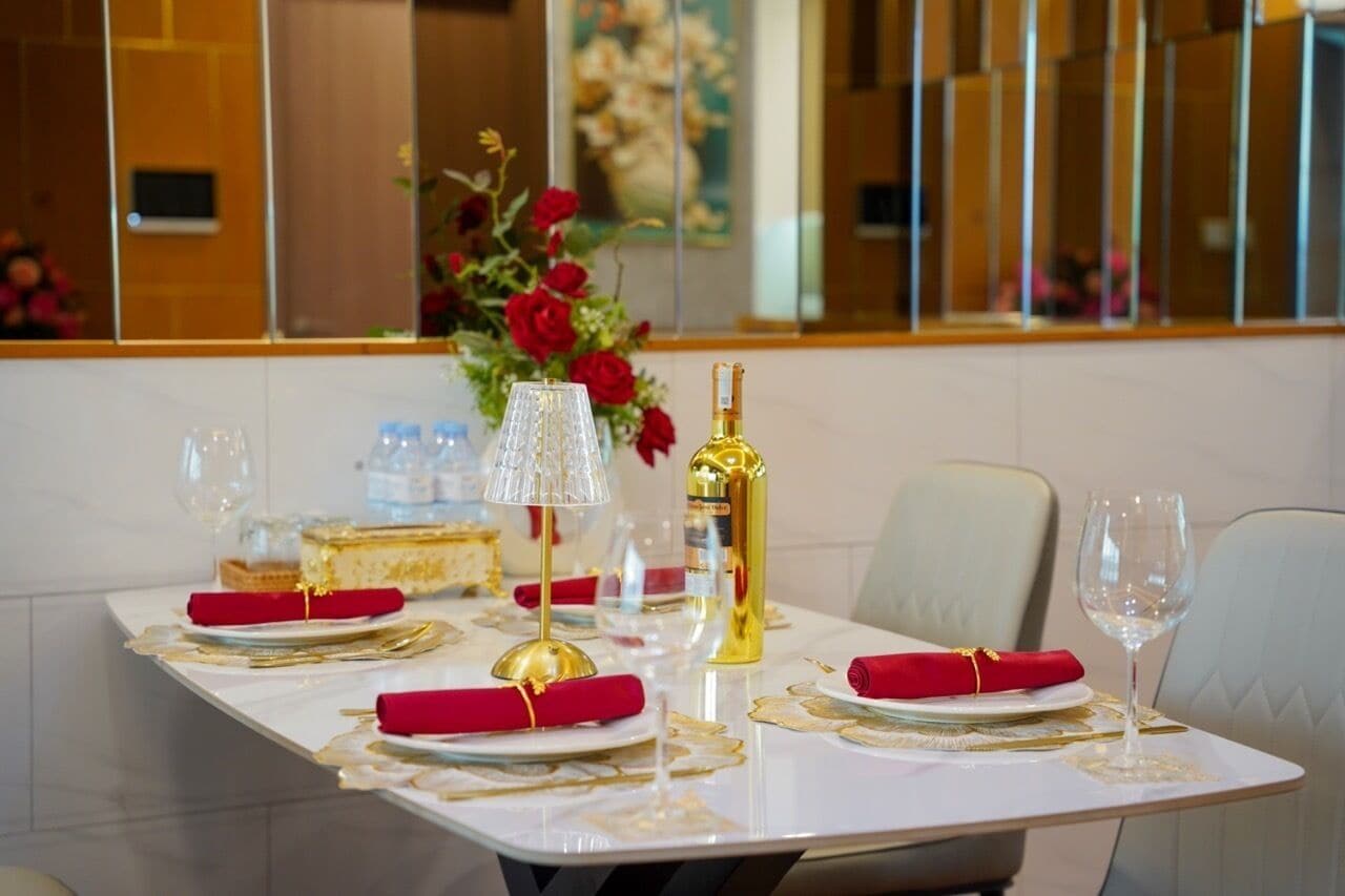 A dining table set with red napkins, gold cutlery, and a bottle of champagne.