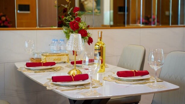 A dining table set with red napkins, gold cutlery, and a bottle of champagne. - Landmark 81 Serviced Apartment - Mariana (Ho Chi Minh City)