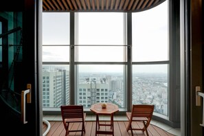 A balcony with a table and two chairs, overlooking a cityscape through large windows. - Landmark 81 Serviced Apartment - Mariana (Ho Chi Minh City)