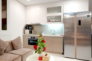 A modern kitchen with stainless steel appliances, a white countertop, and a beige sofa. - Landmark 81 Serviced Apartment - Mariana (Ho Chi Minh City)