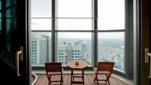 A balcony with two wooden chairs and a small table, overlooking a cityscape through large windows. - Landmark 81 Serviced Apartment - Mariana (Ho Chi Minh City)