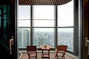 A balcony with two wooden chairs and a small table, overlooking a cityscape through large windows. - Landmark 81 Serviced Apartment - Mariana (Ho Chi Minh City)