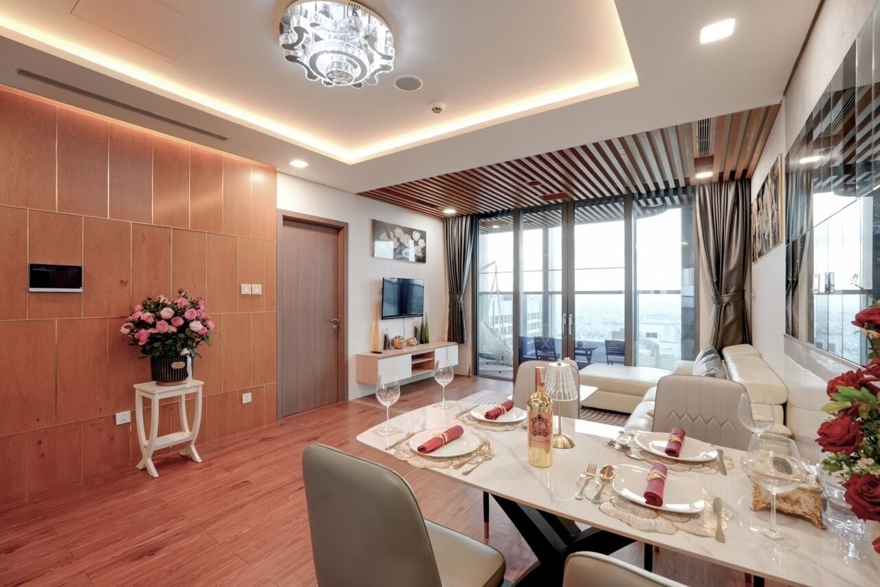 A modern dining area with a wooden floor, a dining table set for four, a chandelier, and a large window with curtains.