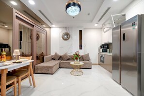 A modern kitchen with a large refrigerator, a dining area with a table and chairs, and a living area with a sofa and decorative items. - Landmark 81 Serviced Apartment - Mariana (Ho Chi Minh City)