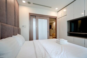 A hotel room with a large bed, a TV mounted on the wall, and a wooden door leading to a bathroom. - Landmark 81 Serviced Apartment - Mariana (Ho Chi Minh City)