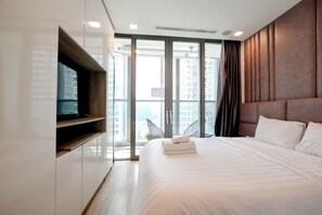Ein modernes Hotelzimmer mit einem großen Bett, einem Flachbildfernseher und Blick auf die Stadt durch raumhohe Fenster.