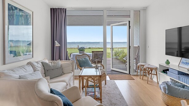 Una sala de estar con un sofá, una mesa, sillas, una televisión y vistas al exterior.