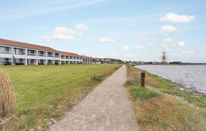 A pathway leading to a building with multiple balconies, a grassy area, and a body of water with a ship in the distance. - Beautiful home in Ebeltoft with WiFi (Ebeltoft)