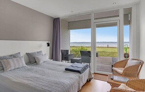 Une chambre avec un grand lit, une chaise, une petite table et une vue sur la mer, accessible par une porte-fenêtre coulissante.