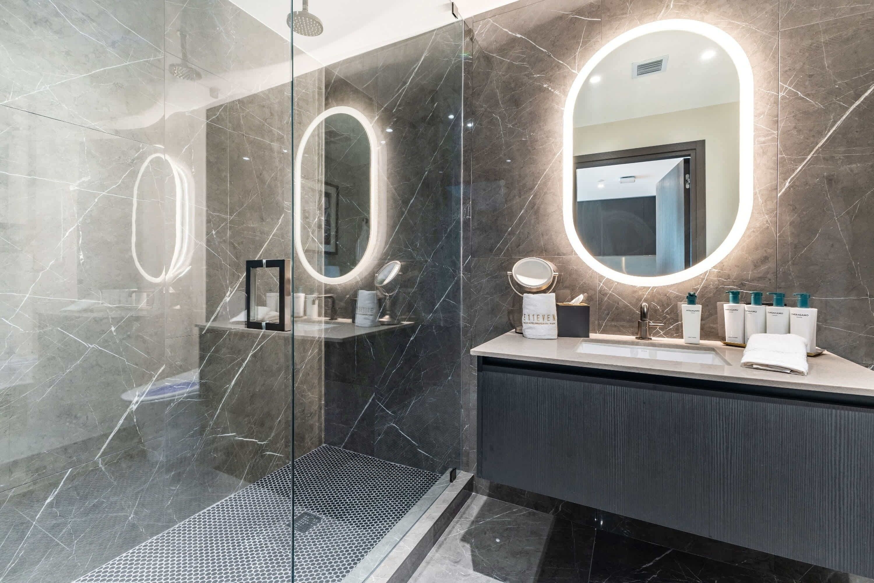 Een moderne badkamer met een douchecabine van glas, een wastafel met spiegel en toiletartikelen.