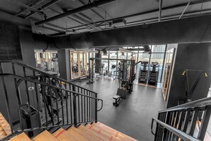 Ein Fitnessstudio mit Trainingsgeräten, einer Treppe und großen Fenstern.