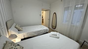 Een hotelkamer met twee enkele bedden, een spiegel, een raam met dunne gordijnen en een deur naar een badkamer.