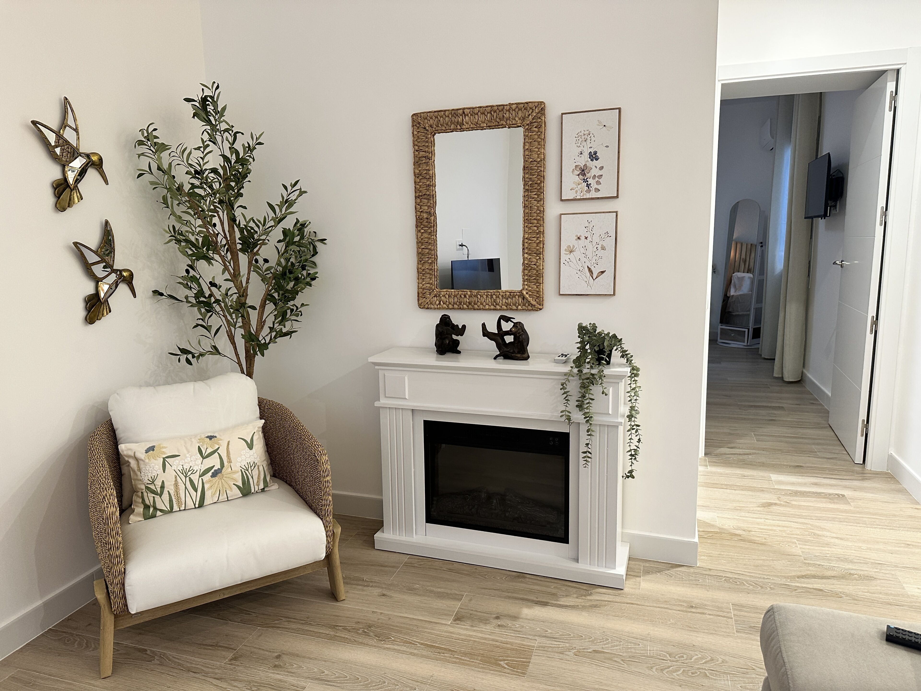 Una sala de estar con chimenea blanca, un sillón de mimbre con cojines estampados, un espejo grande y obras de arte en la pared.