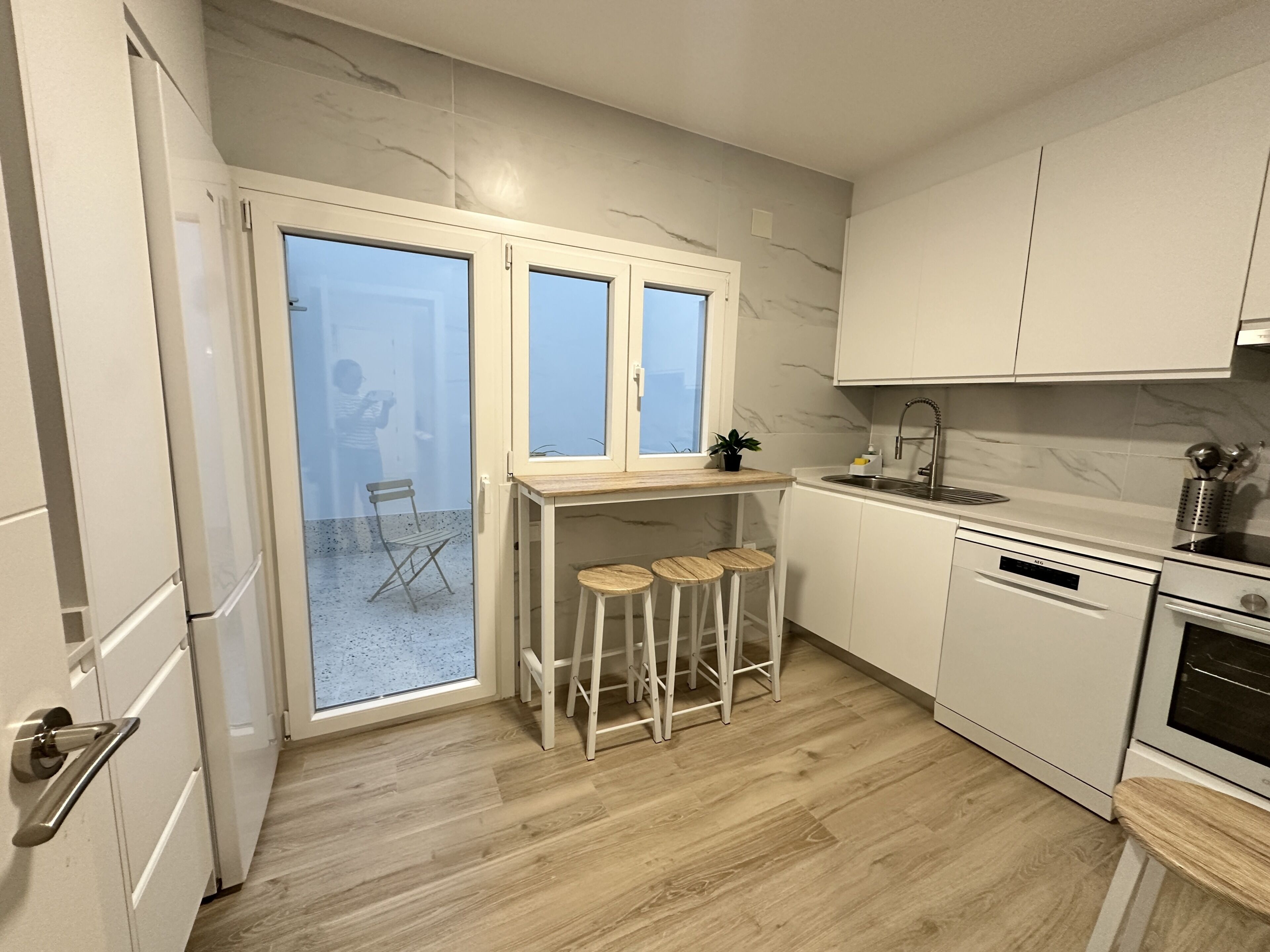 Een moderne keuken met witte kasten, een ingebouwde oven, een spoelbak en een raam met uitzicht op een balkon.