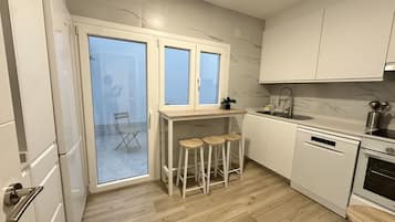 Een moderne keuken met witte kasten, een ingebouwde oven, een spoelbak en een raam met uitzicht op een balkon.