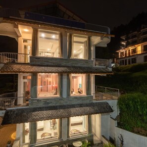 A multi-story building with balconies, large windows, and a well-lit interior. - DLS Spring Valley Resort, Dharamshala (Dharamshala)