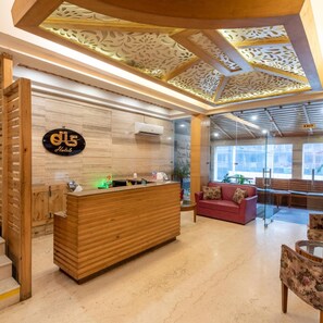 A hotel reception area with a wooden reception desk, a sign with the hotel's name, a glass wall, and a red sofa. - DLS Spring Valley Resort, Dharamshala (Dharamshala)
