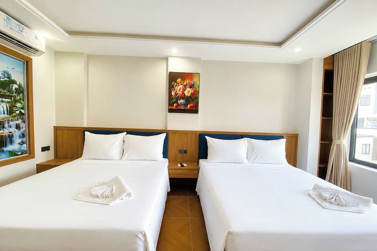 A hotel room with two beds, a painting on the wall, and a window with curtains.