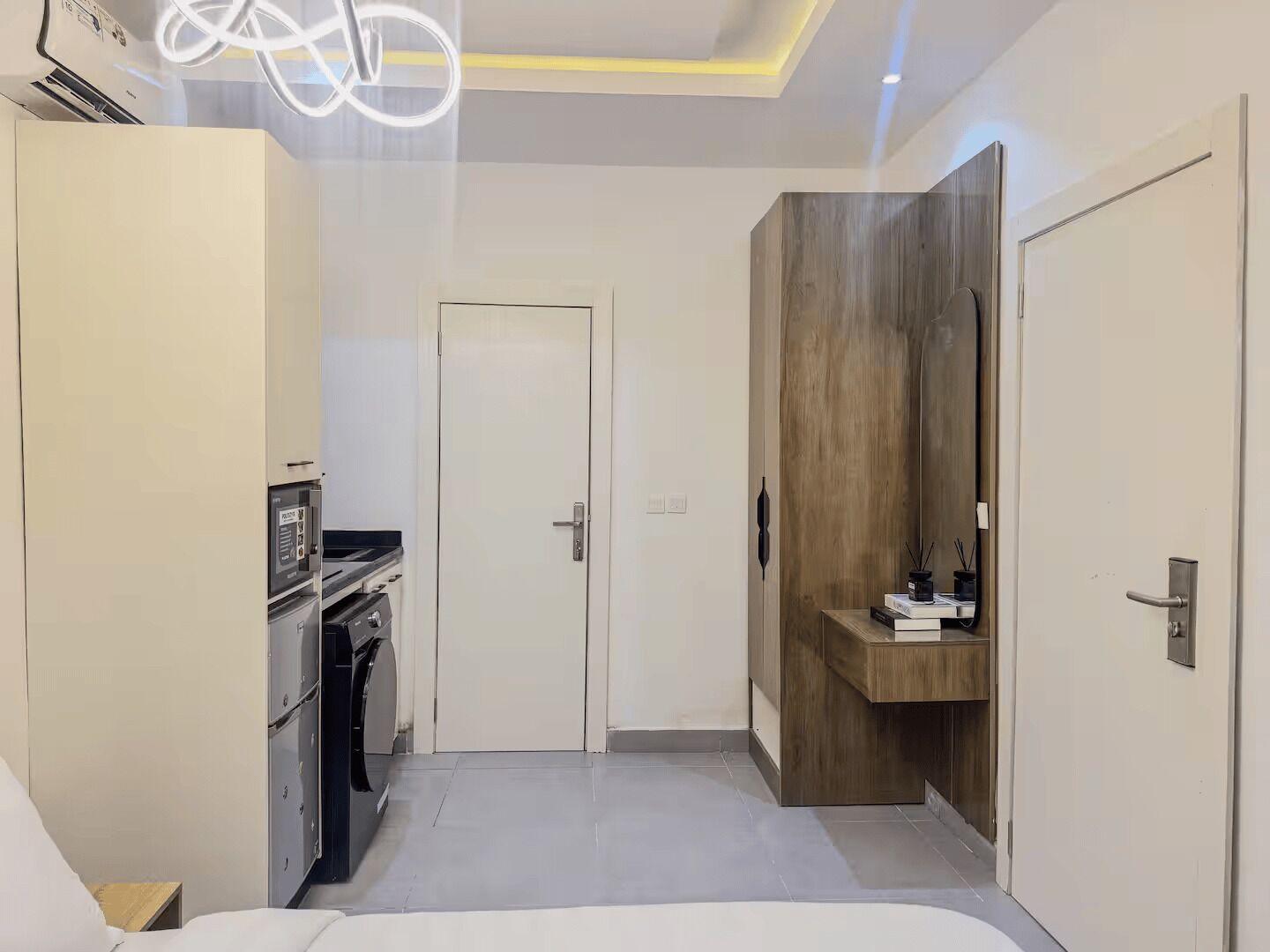 A modern hotel room with a kitchenette, a wooden vanity, and a large bed.