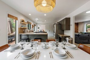 A modern dining area with a long table set for a meal, a kitchen in the background, and a seating area with a sofa. - West Sedona retreat with 4 bedrooms, hot tub, and Red Rock views. (Sedona)