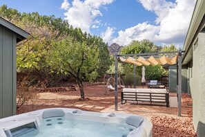Ein Garten mit Whirlpool, Gartenmöbeln, einer Pergola und einem Blick auf die Berge.
