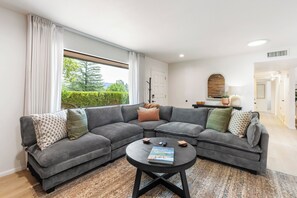 A modern living room with a sectional sofa, a coffee table, and a view of a green landscape through large windows. - West Sedona retreat with 4 bedrooms, hot tub, and Red Rock views. (Sedona)