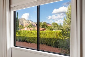 Ein Fenster mit Blick auf einen Berg, einen gepflegten Heckenstreifen und einen klaren Himmel.