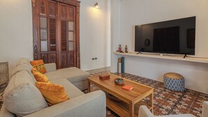 Een woonkamer met een bank, een salontafel, een televisie op een dressoir en een vloer met een patroon.