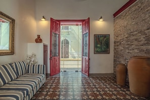 A room with a striped sofa, a tiled floor, a red door with decorative metalwork, a brick wall, and a framed picture. - Colonial House in Downtown  (Mérida)