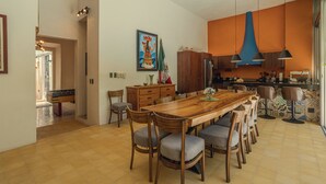 Een ruime eethoek met een houten tafel en stoelen, een keuken met moderne apparatuur, en een plafondventilator.
