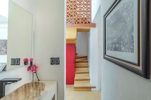 A bathroom with a wooden basin, a mirror, a pink flamingo decoration, and a red door leading to a staircase. - Colonial House in Downtown  (Mérida)