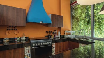 Una cocina moderna con un horno negro, una campana extractora azul y un ventanal con vistas a zonas verdes.