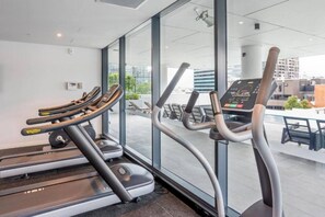A gym with treadmills and exercise equipment, large windows, and a view of the cityscape. - Luxury Meets Lifestyle (Fortitude Valley)