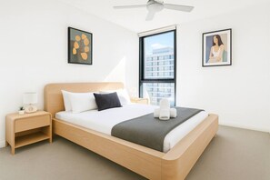 A modern hotel room with a large bed, a nightstand, a window with a view of buildings, and two framed pictures on the wall. - Luxury Meets Lifestyle (Fortitude Valley)
