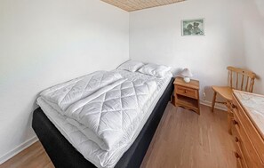 Ein Einzelbett mit weißer gesteppter Decke, ein Nachttisch mit Lampe sowie ein Holzstuhl.