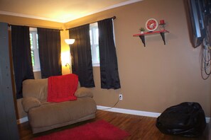A living room with a sofa, a red throw blanket, a black bag, and a wall-mounted clock.