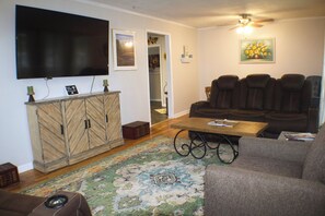 A living room with a flat-screen TV, a sofa, a coffee table, and a patterned rug.