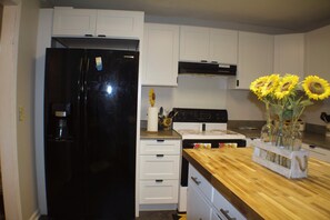 A kitchen with white cabinets, a black refrigerator, a wooden countertop, and a vase with sunflowers. - Spacious 4-bedroom house in charming Ringgold with big yard and pet friendly. (Ringgold)