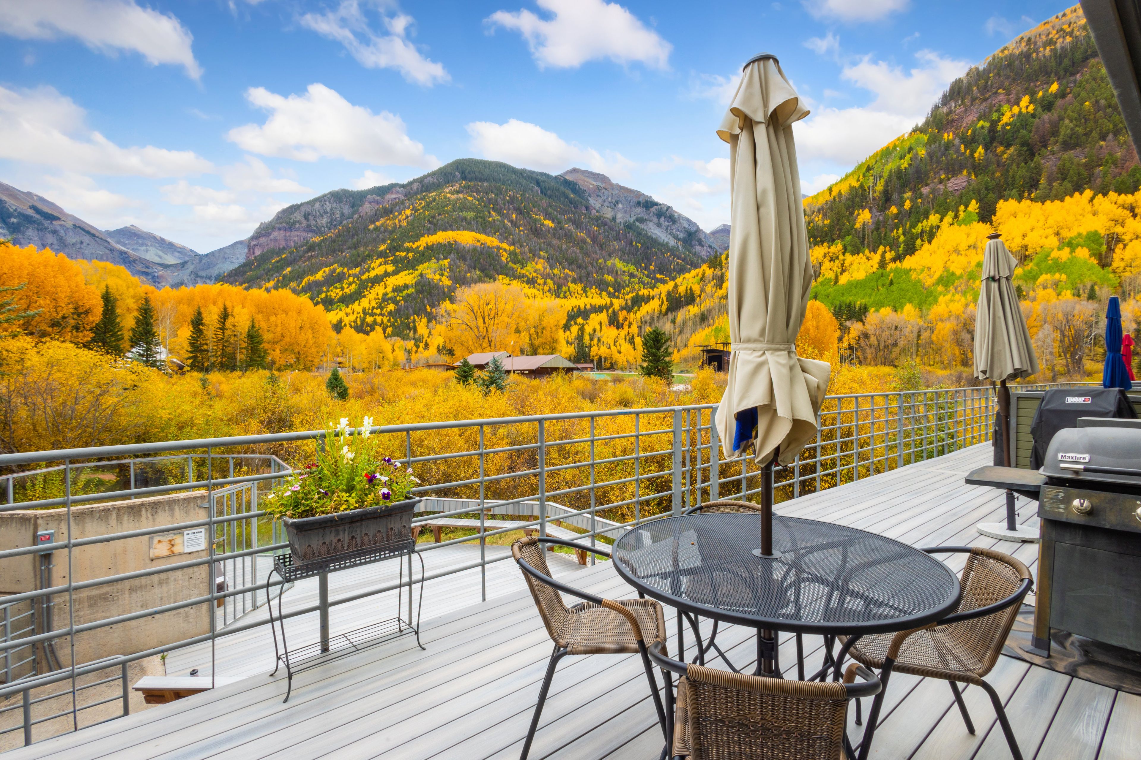 A deck with outdoor furniture, a grill, and a view of a mountainous landscape with autumn foliage.