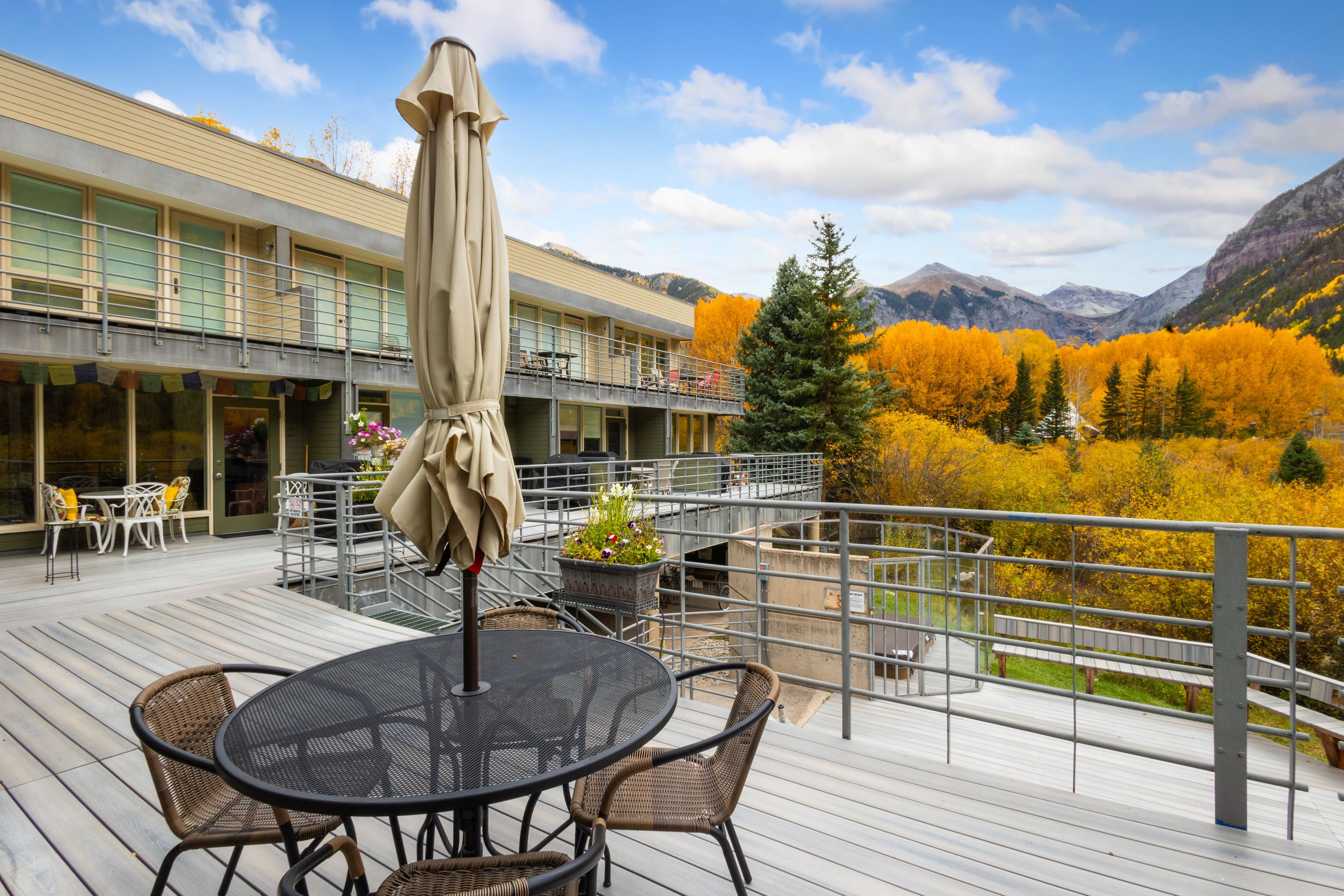 Un balcon d  ’hôtel avec des sièges d’extérieur, une vue sur le feuillage automnal et des montagnes en arrière-plan.