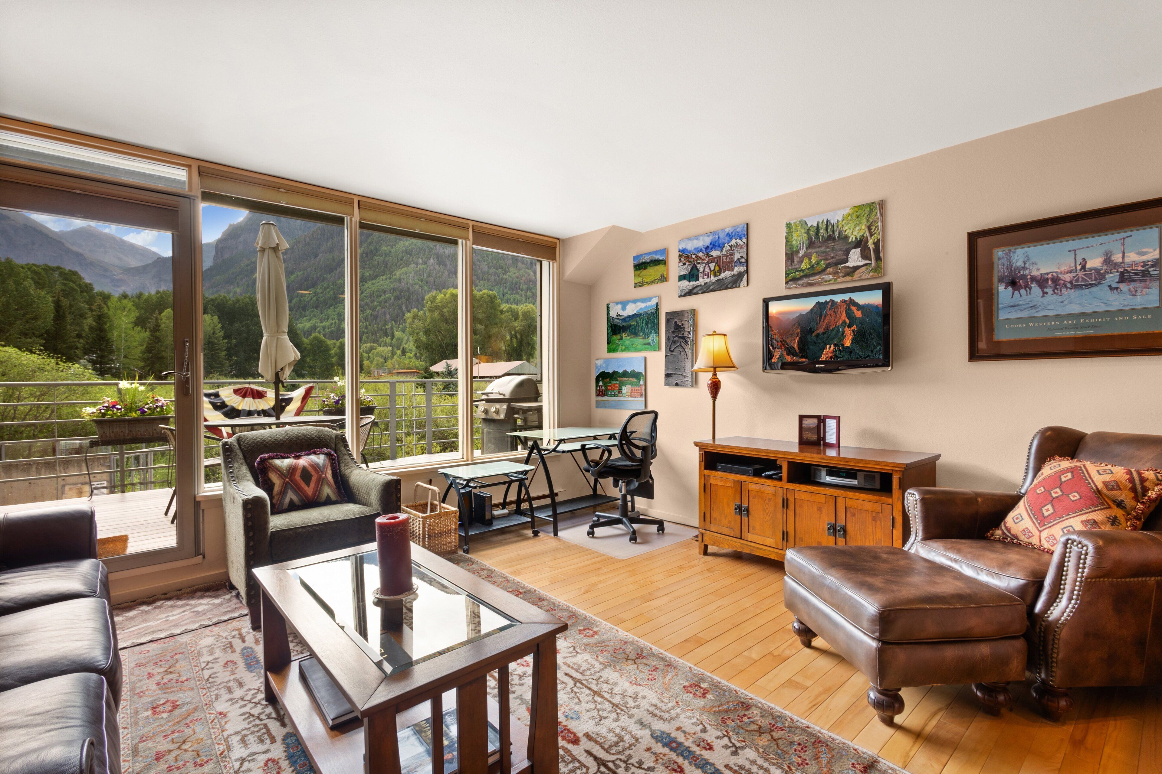 A spacious living room with a large window overlooking a mountainous landscape, a dining area with a table and chairs, and a cozy seating area with a leather sofa and armchairs.