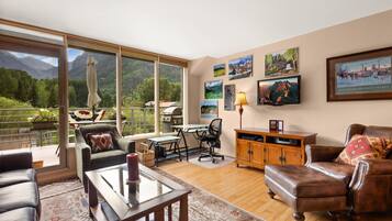 A spacious living room with a large window overlooking a mountainous landscape, a dining area with a table and chairs, and a cozy seating area with a leather sofa and armchairs.