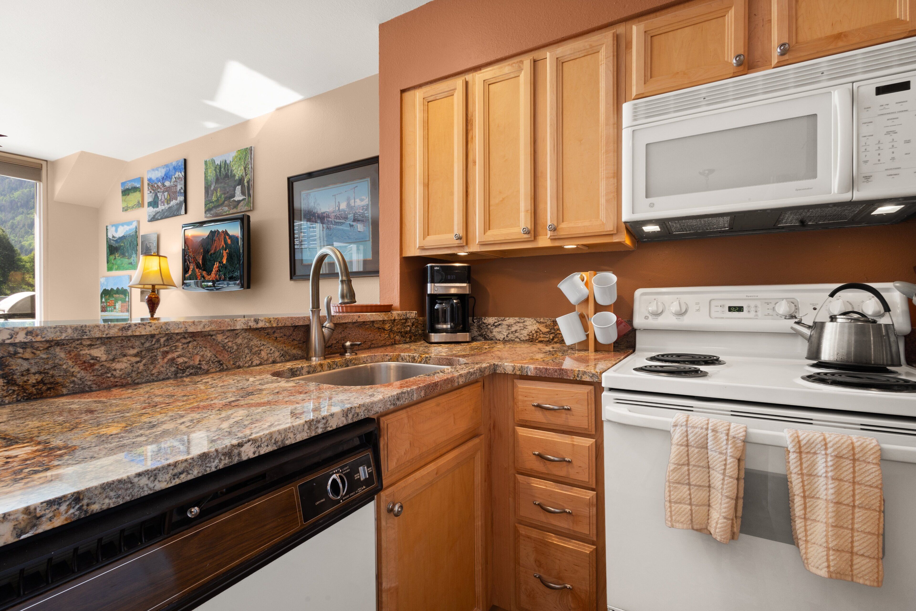 A kitchen with granite countertops, wooden cabinets, a white stove, and a microwave.