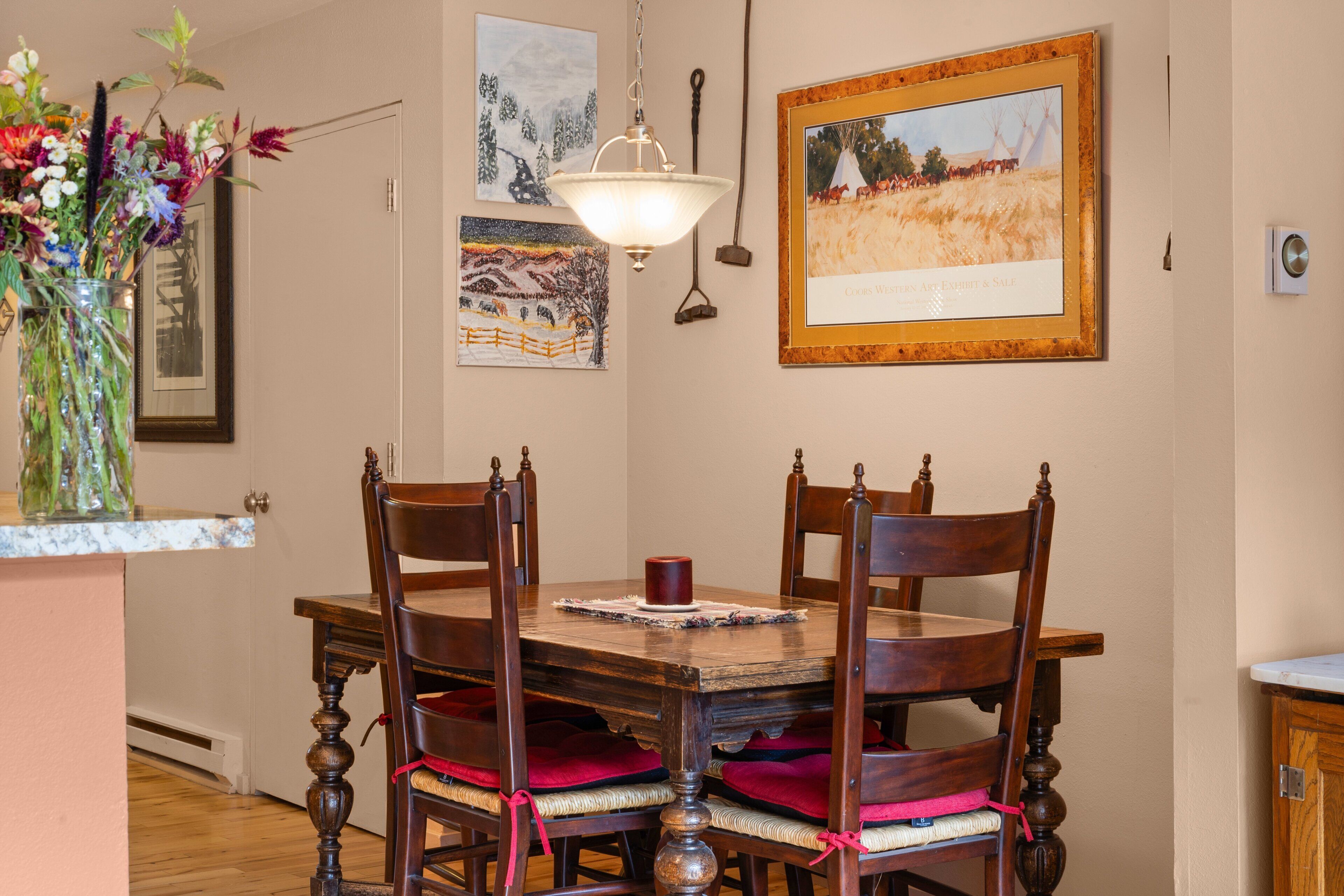 Un comedor con una mesa y sillas de madera, un florero con flores y obras de arte en las paredes.
