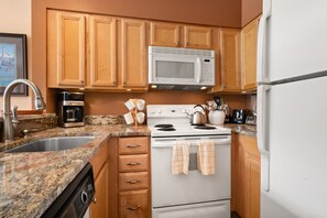 Una cocina con armarios de madera, microondas, estufa, fregadero y varios electrodomésticos.