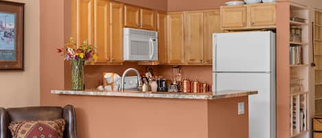 A compact kitchen with wooden cabinets, a microwave, a refrigerator, and a coffee maker.