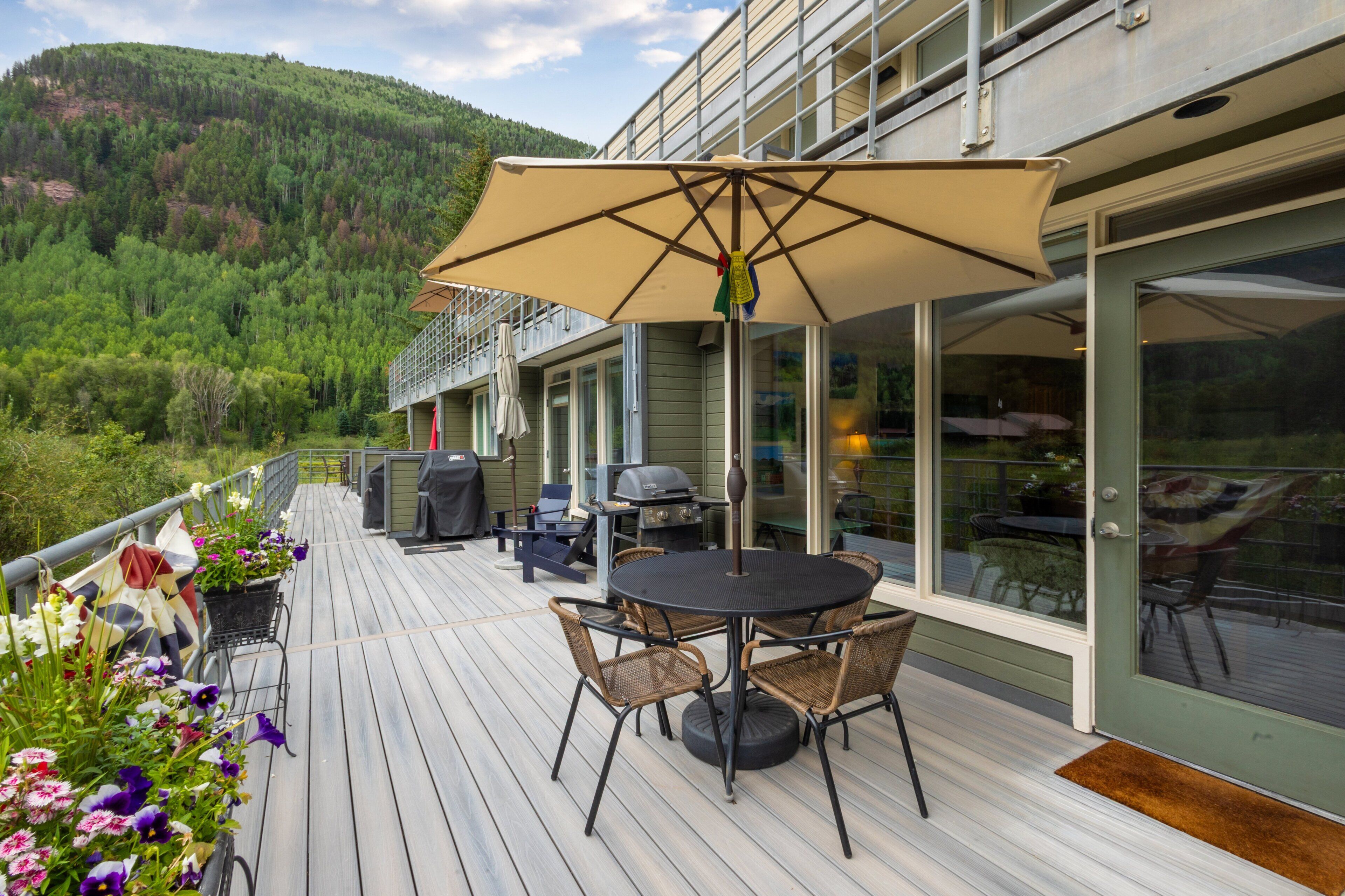 Eine Terrasse mit Gartenmöbeln, einem Grill und Blick auf einen bewaldeten Hang.